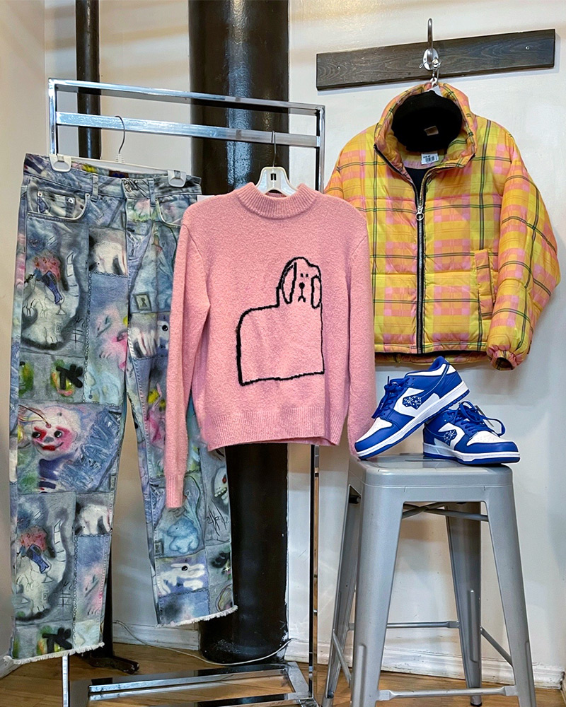 Rack of clothing with jeans,  sweater, jacket and a pair of sneakers sitting on a stool