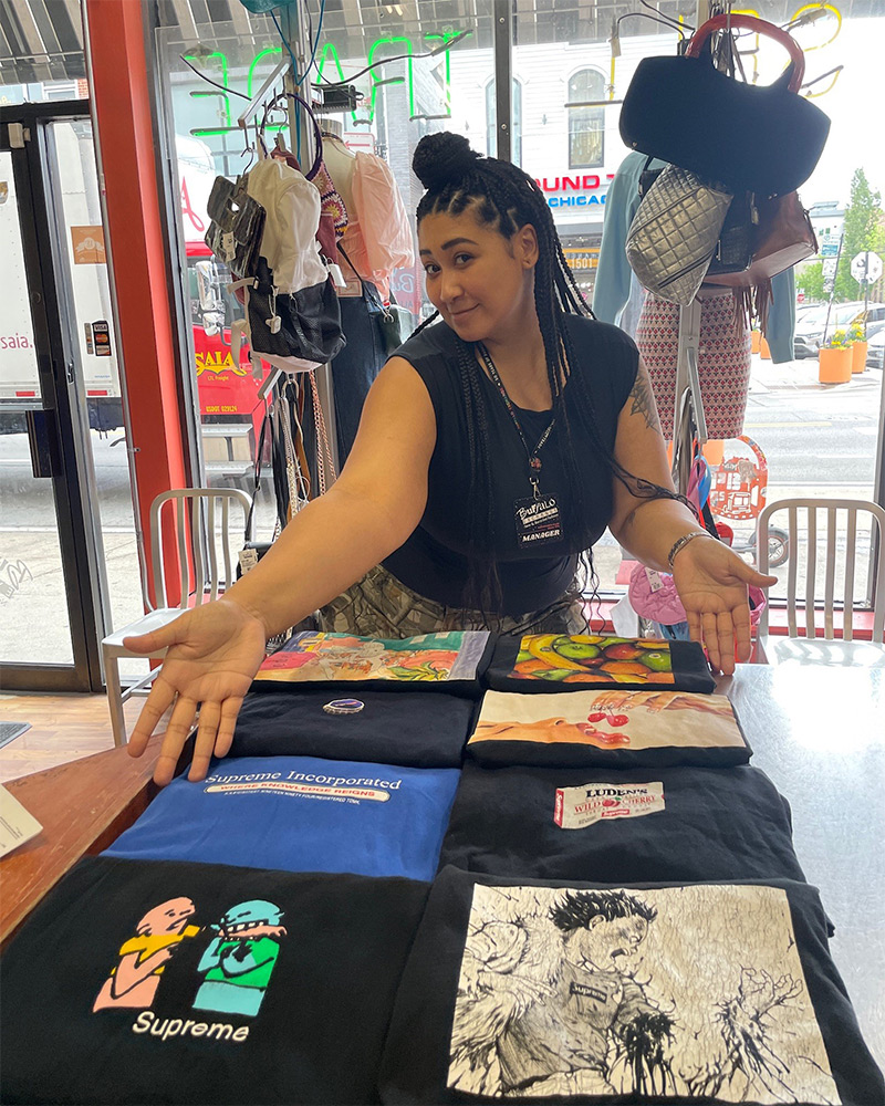 Manager poses with arms open gesturing to graphic tees displayed on table