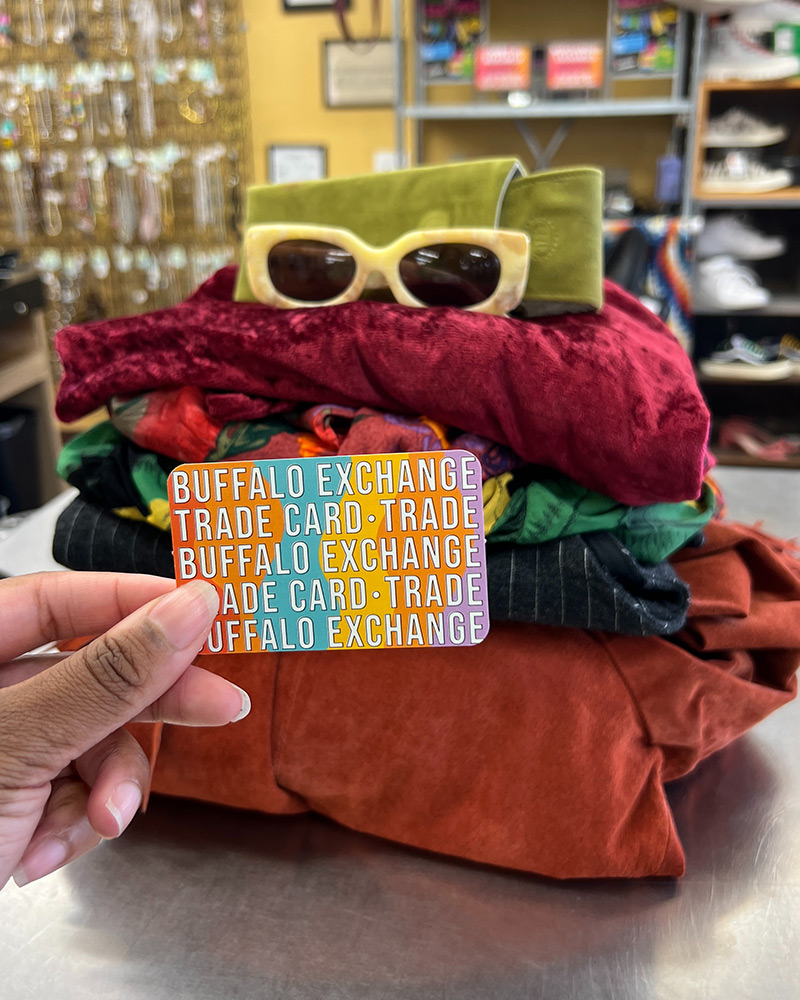 Stack of clothing with hand holding Buffalo Exchange trade card