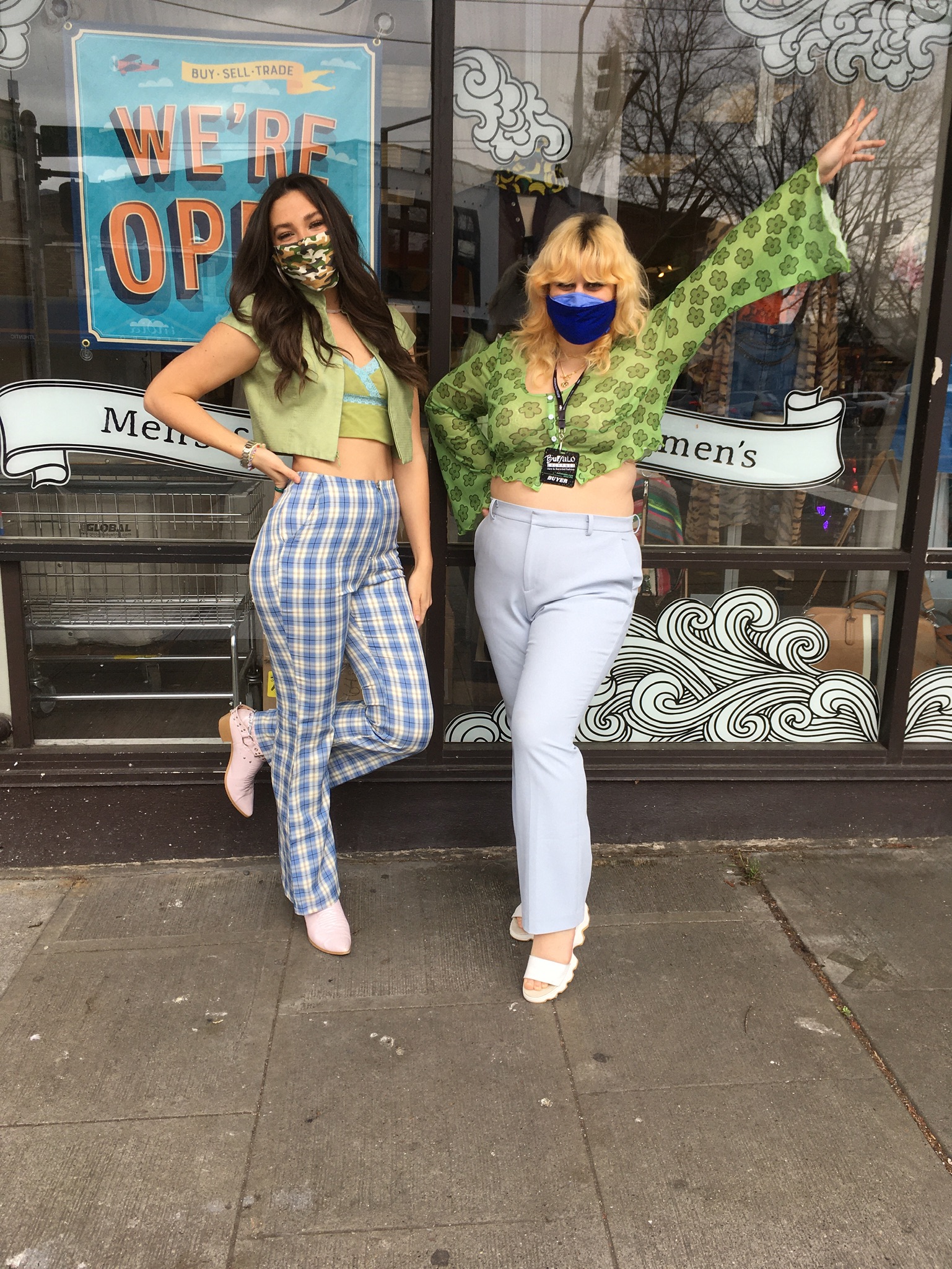 Two people, one wearing an olive green cardigan set and checkered grey denim, the other in a green mesh top and grey slacks