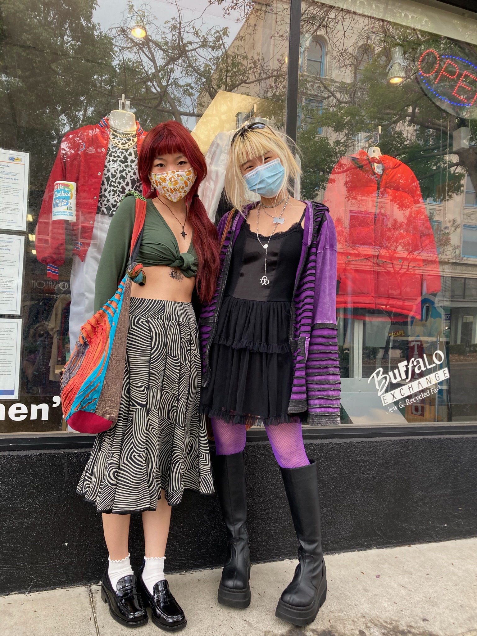 Two people wearing grunge-style clothing such as a zebra print skirt, loafers, black and purple striped sweater, and purple fishnets