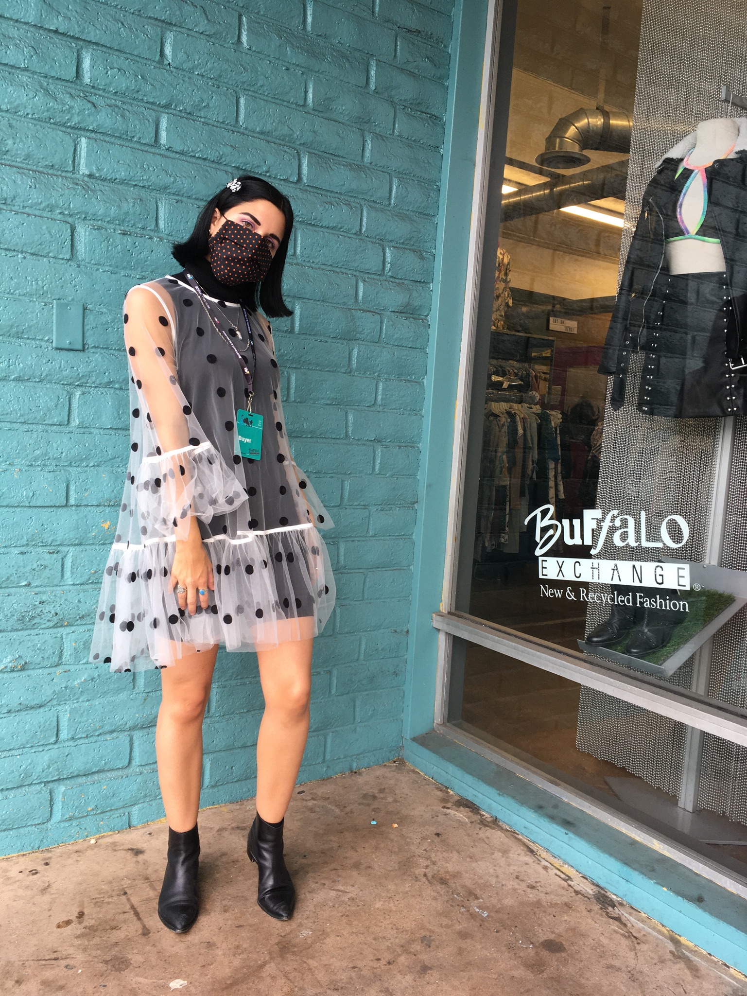 Woman standing in doorway to Buffalo Exchange wearing black dress with sheer overlay polka dot dress