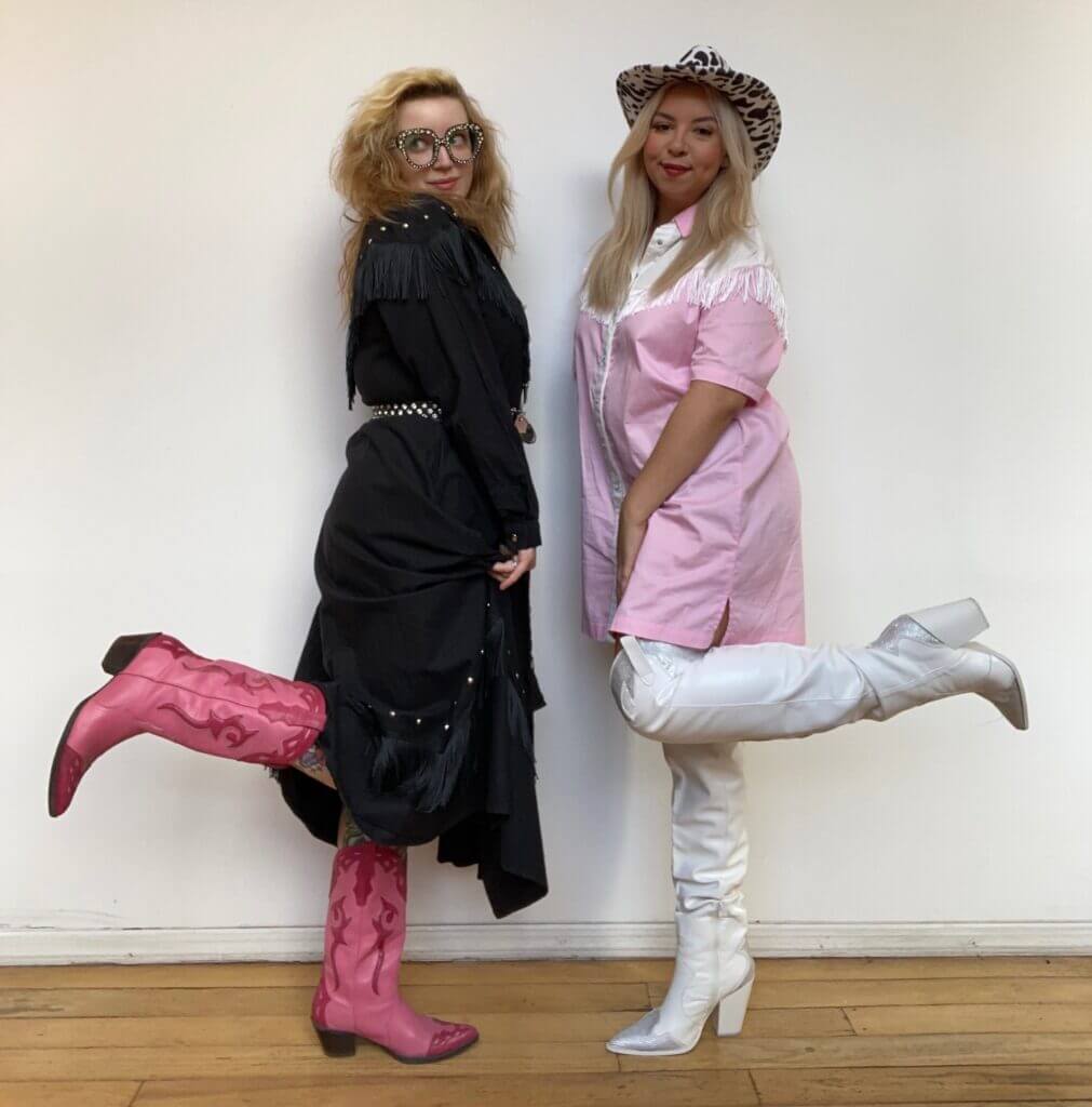 Two people wearing pink and black cowboy costumes with fringe, cowboy hats, and cowboy boots