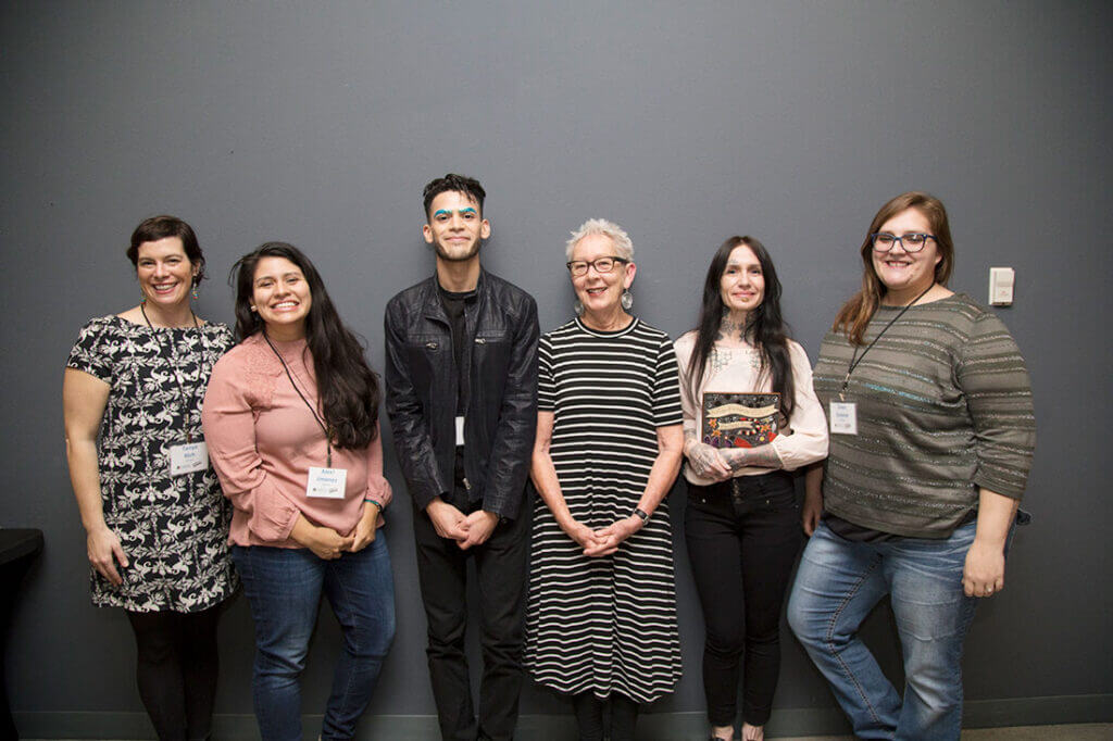 6 people standing in front of a wall smiling