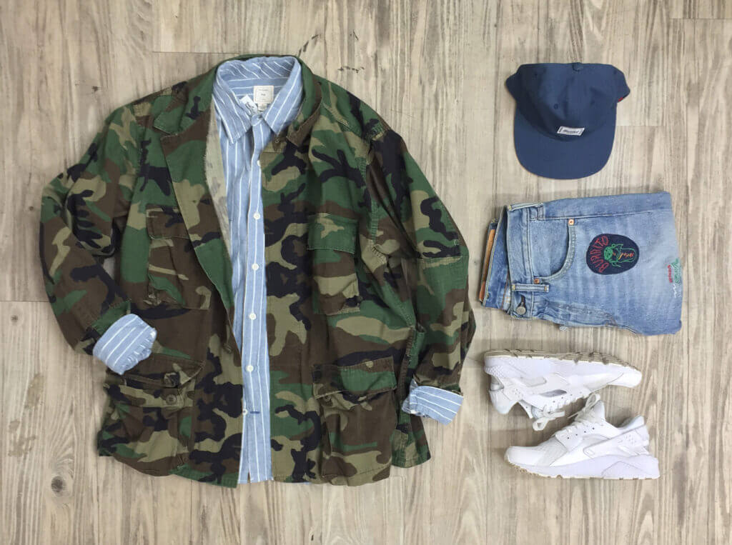 camouflaged jacket over a blue and white striped shirt, blue baseball cap, folded blue jeans with patch and white sneakers