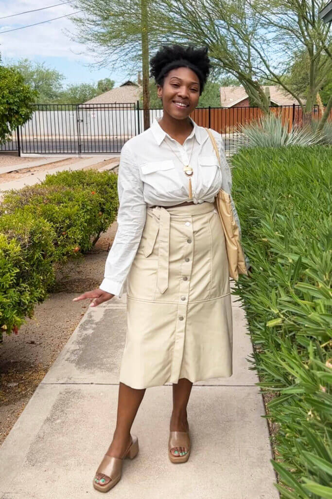 Person standing on sidewalk wearing tan midi skirt and white blouse