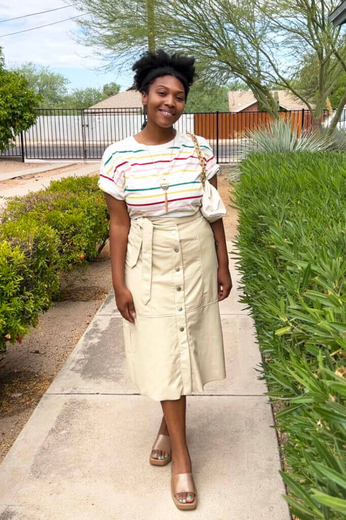 Person standing on sidewalk wearing tan midi skirt and striped t-shirt