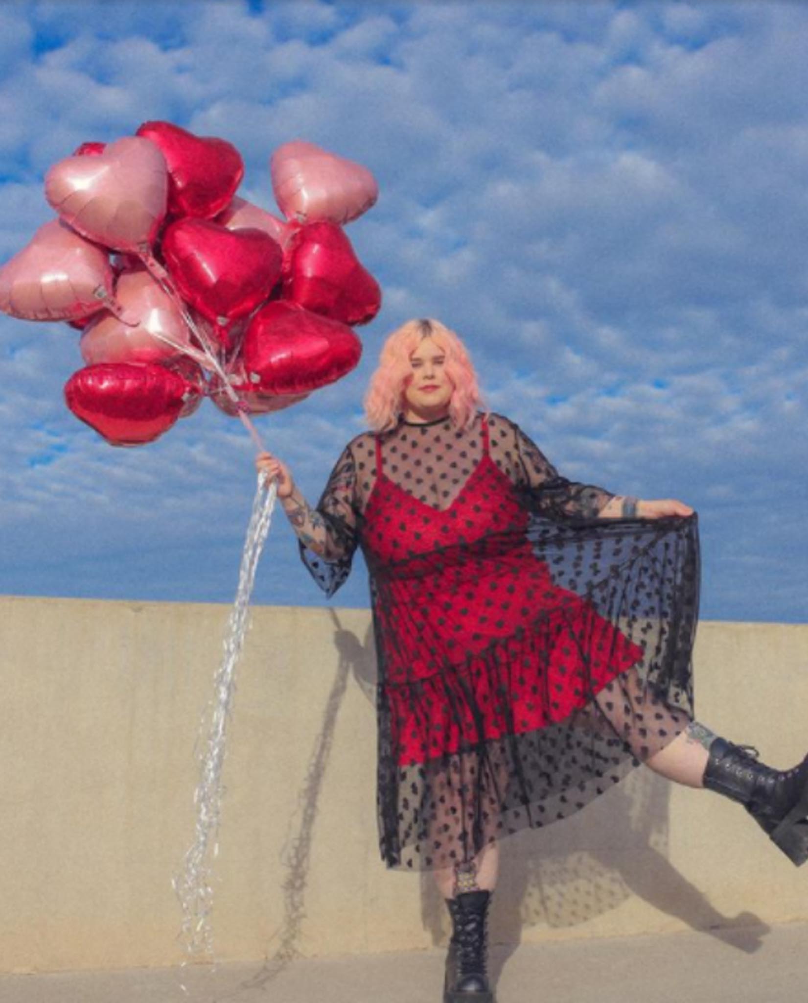 Caelyn in a red dress with black mesh holding heart shaped balloons