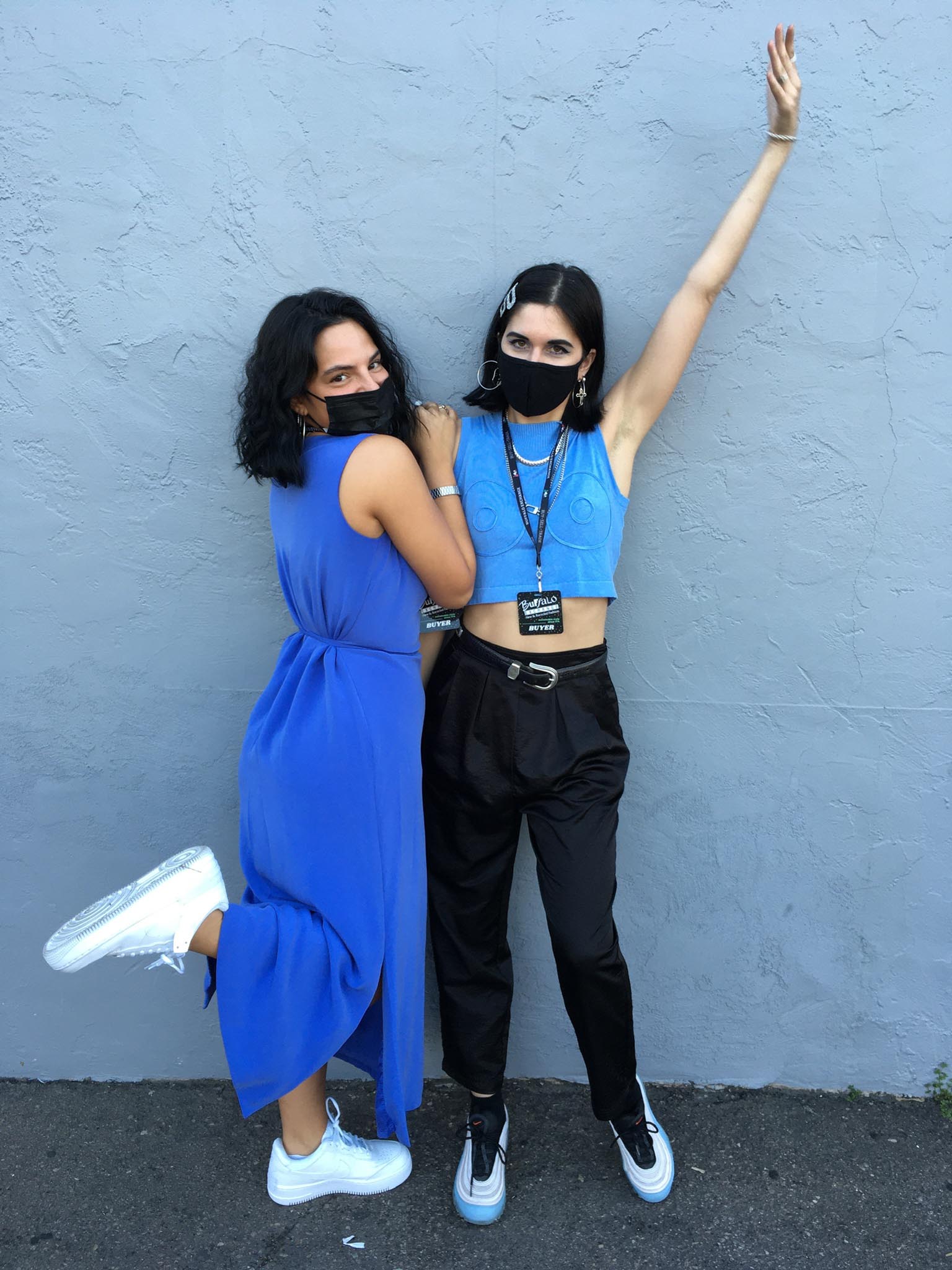 A person wearing a blue midi dress and white sneakers with another person in a blue cropped tank, black pants, and Nike Air Max sneakers