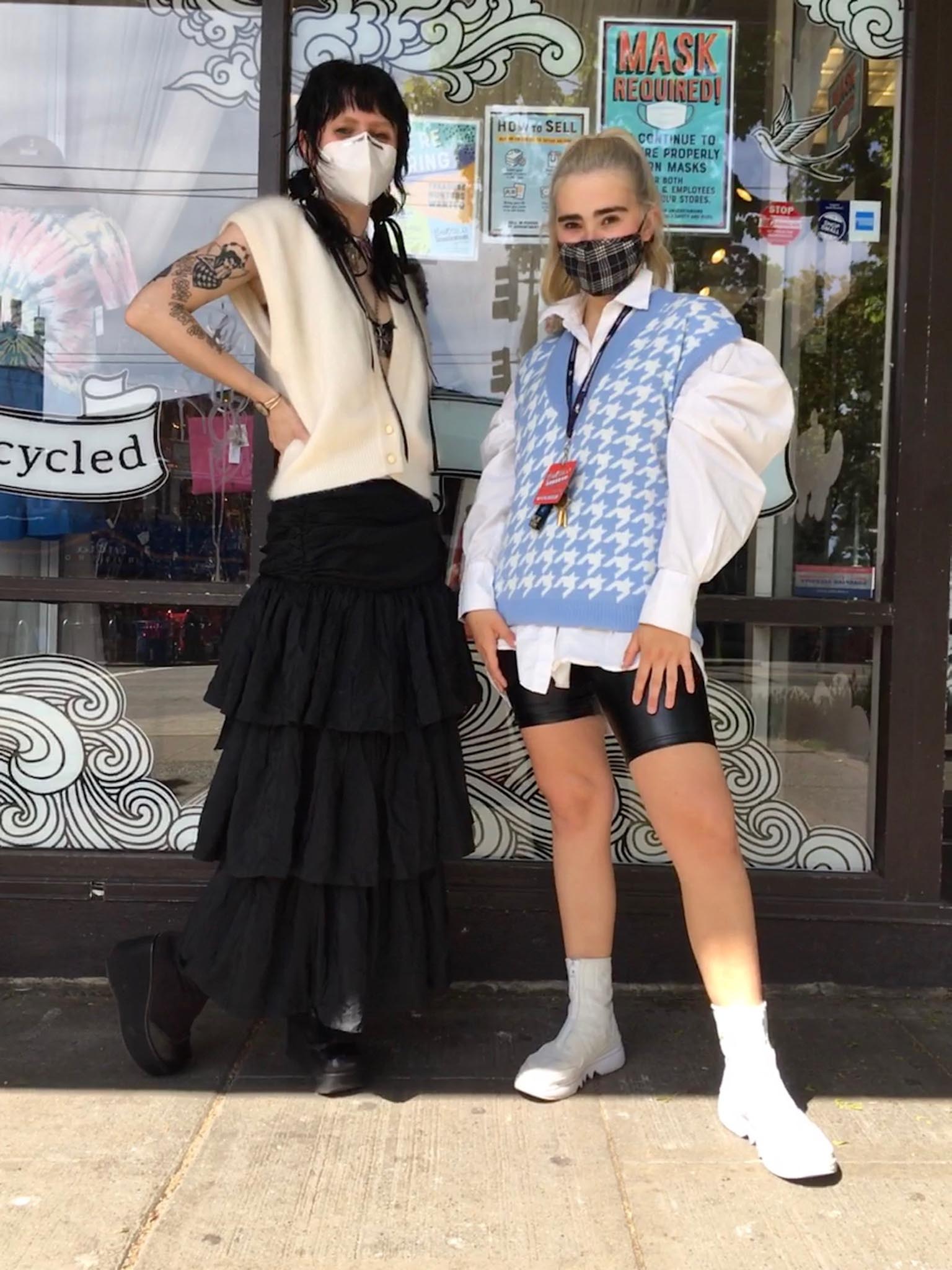 Two people pose in front of a shop window wearing fuzzy sweater vests