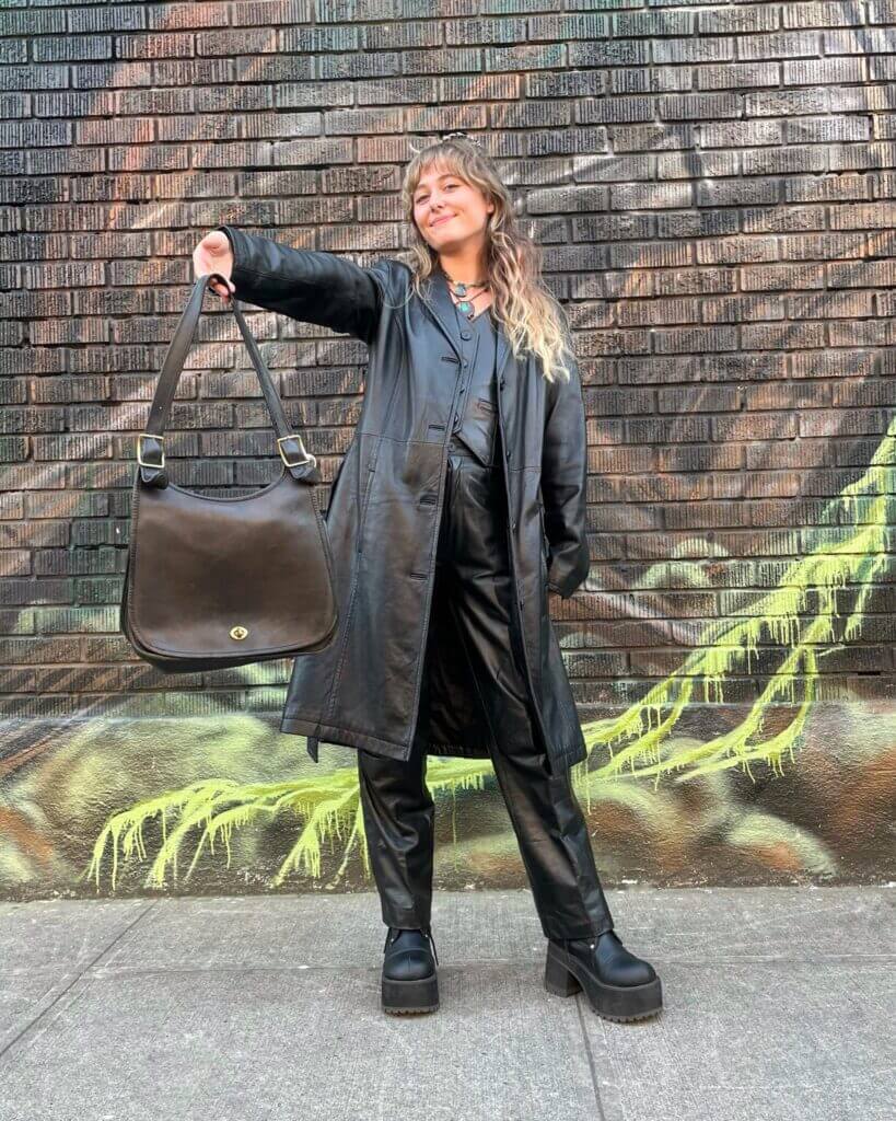 A woman wearing all black leather holding a black vintage Coach bag