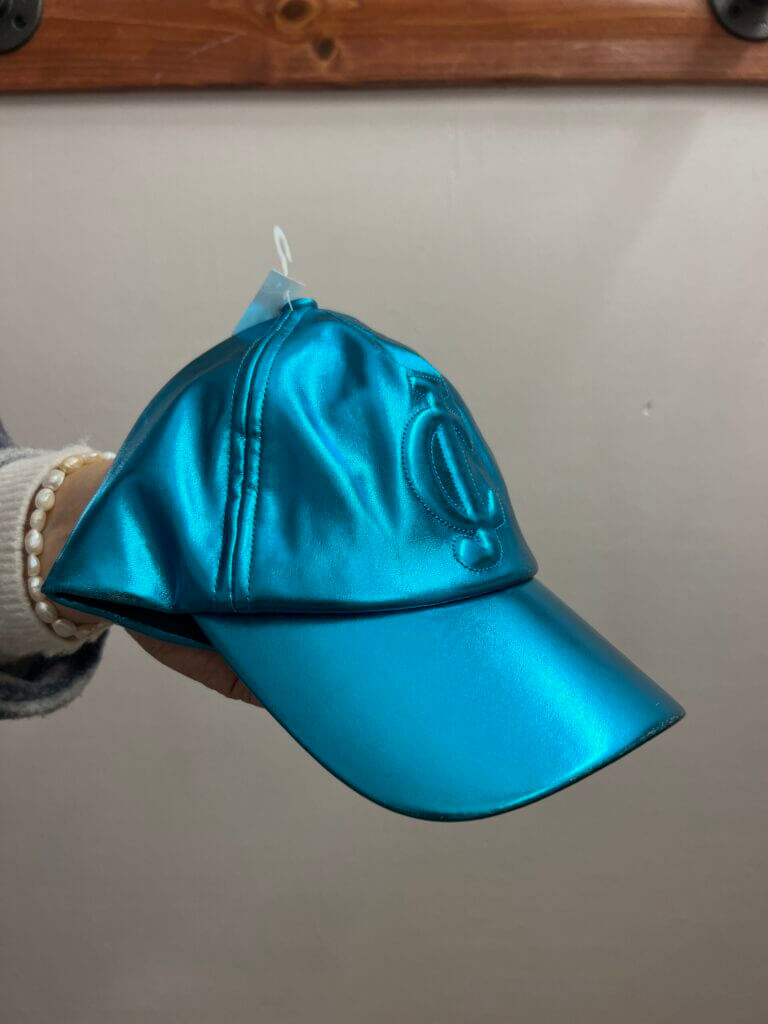 close up of a hand holding a Juicy Couture metallic blue baseball cap