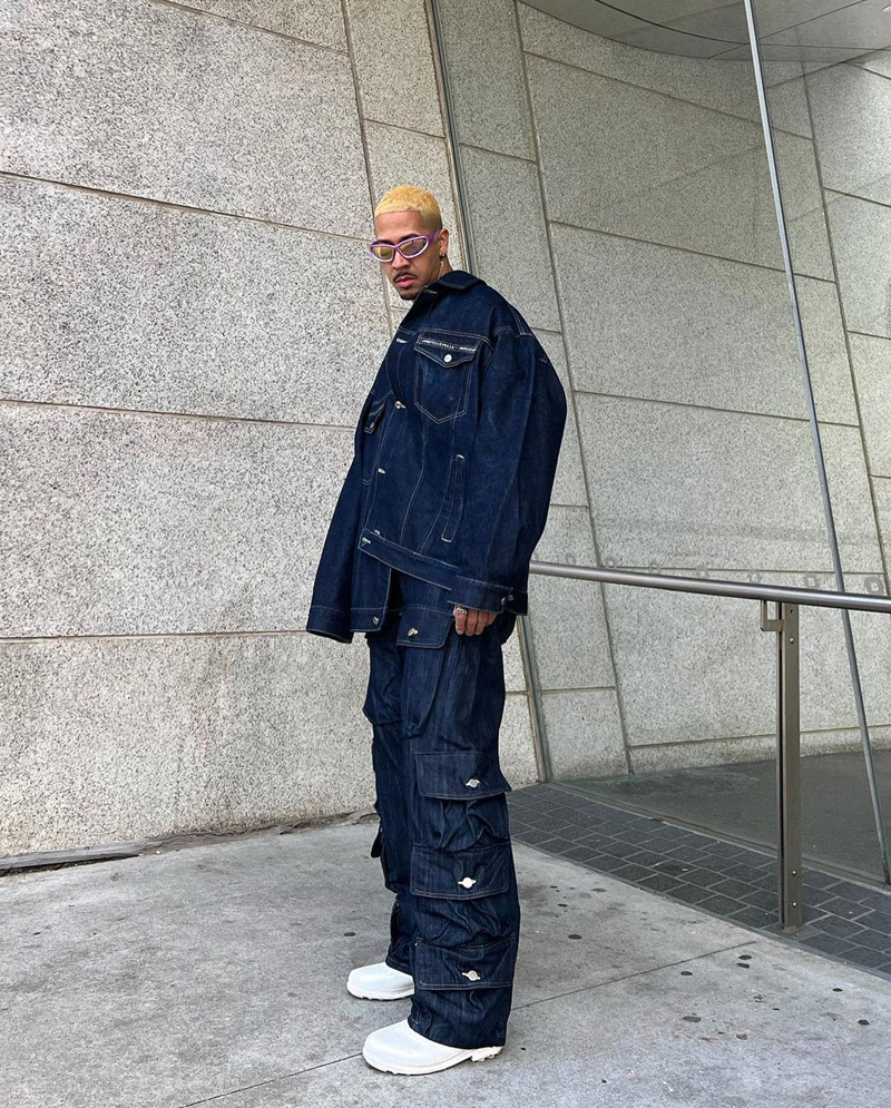 Customer @jayrsantana wearing a boxy denim jacket, matching denim cargos, metallic pink shield glasses, and white sneakers