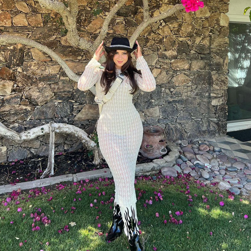 @kendramcleish wearing a black cowboy hat, sheer white dress, and white cowboy boots with black flame details.