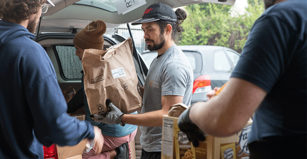 Volunteers unloading paper bags of food from trunk of car