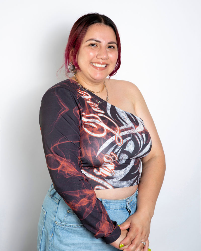 A headshot of Monique wearing a graphic one shoulder top and jeans