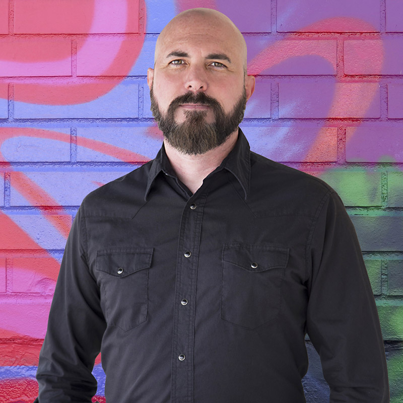 Joe wearing black shirt in front of colorful brick wall