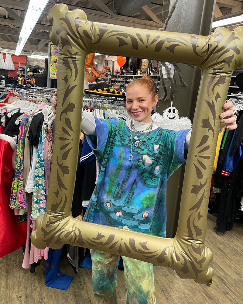 A person wearing handpainted top and pants to resemble watercolor painting holds inflatable picture frame