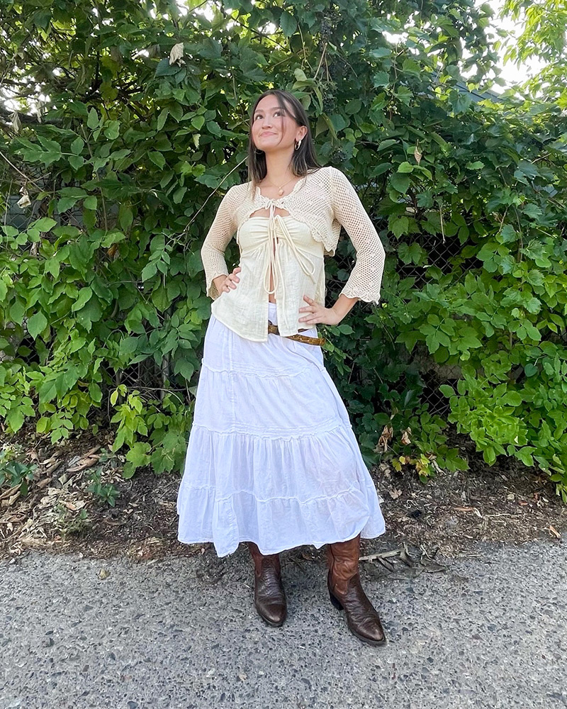 Blog-1-Edited Woman wearing cream sweater and white maxi skirt stands in front of green bush