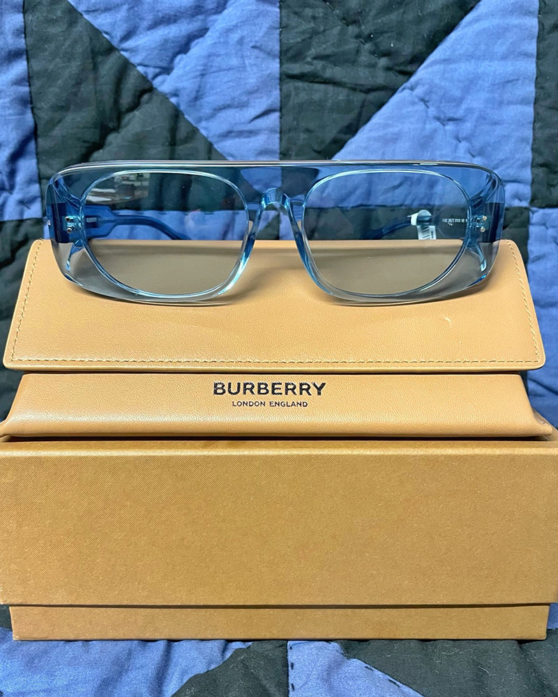 Blog-21-Edited Blue tinted Burberry sunglasses sit on top of their box with a quilt in the background