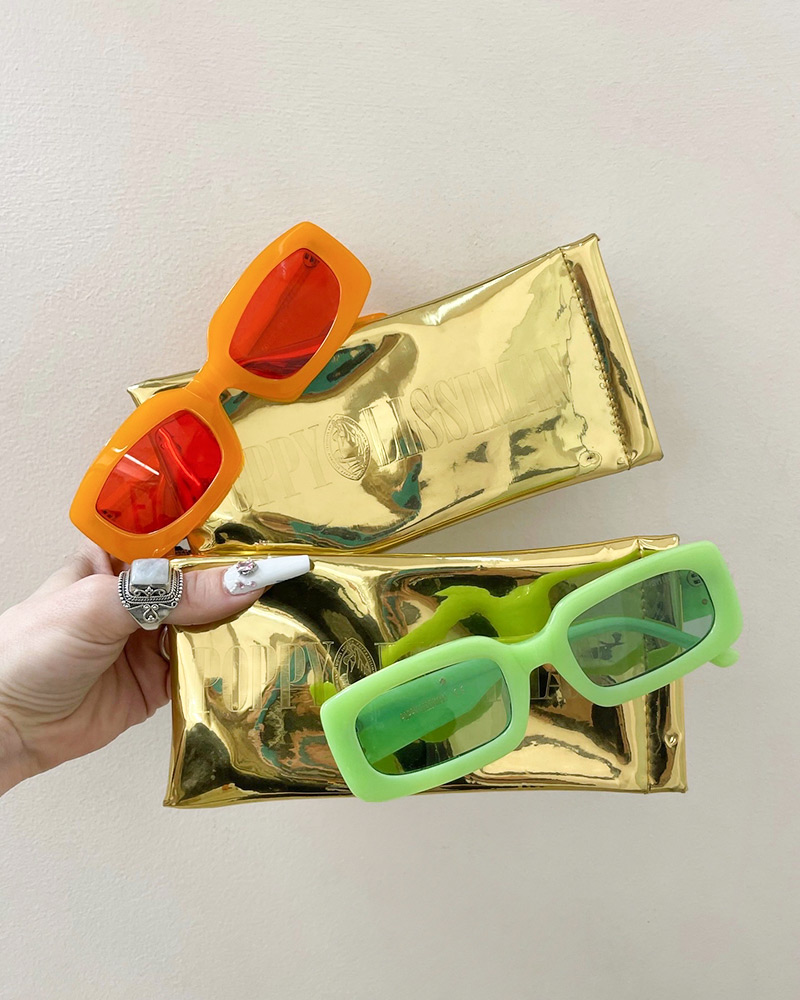 Blog-22-Edited A hand holds two pairs of Poppy Lissman orange and green sunglasses and their gold foil carrying cases