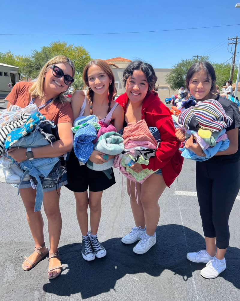 eday blog pic 1 resized a group of friends standing in parking lot smile while holding piles of clothing
