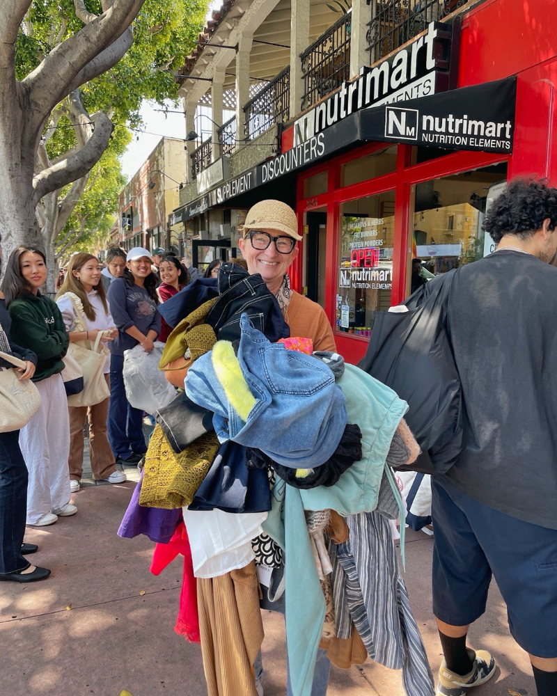 eday blog pic 9 resized person standing in front of line of shoppers on sidewalk holds pile of clothes