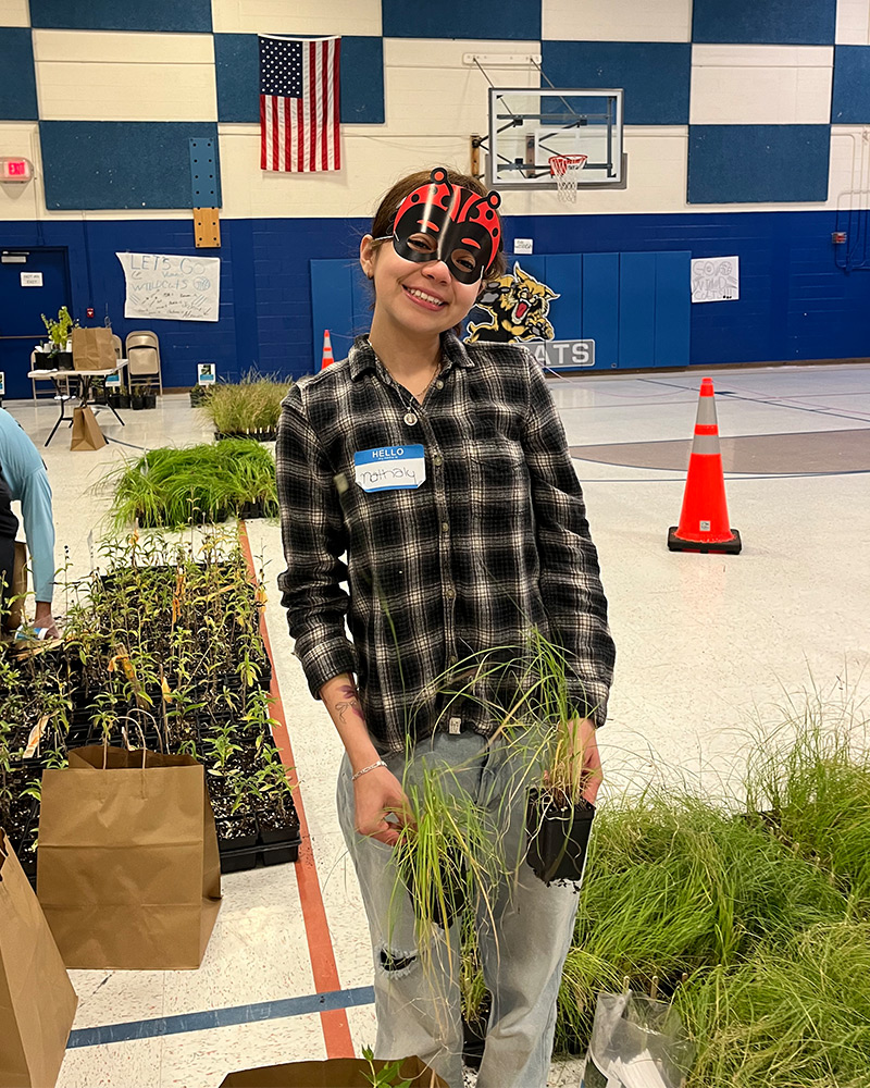Community member smiling and wearing ladybug mask while working with plants