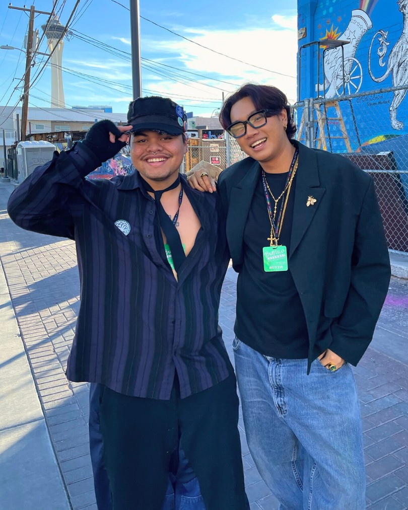 Two people laughing wearing business casual pieces like an oversized shirt and blazer styled with alt accessories including fingerless gloves, chains and baggy jeans