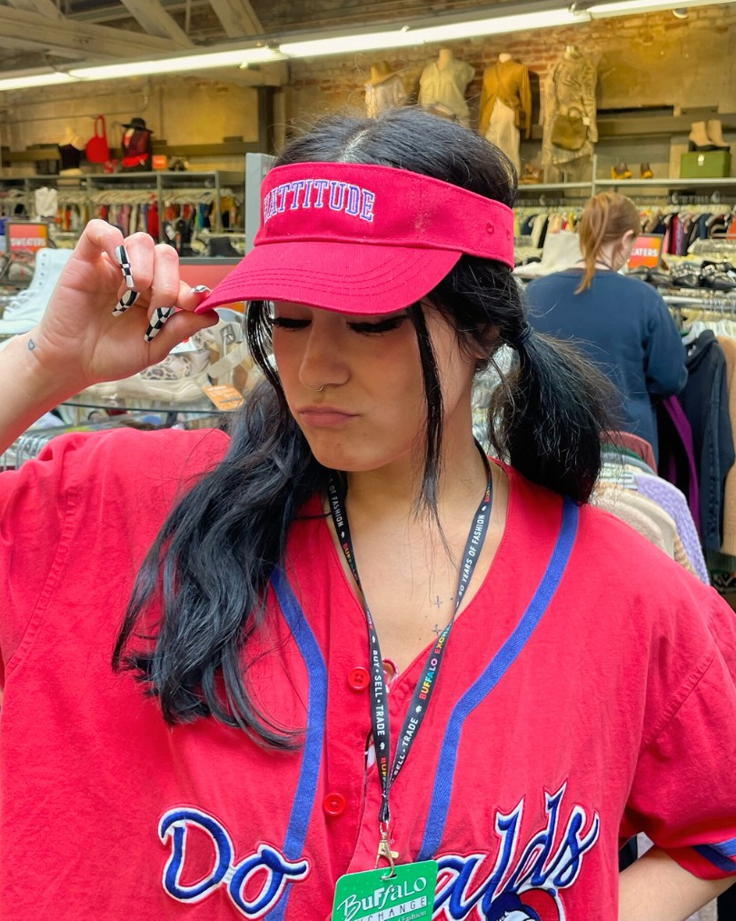 Employee at Buffalo Exchange in pigtails wearing a sporty red visor with "Hattitude" embroidered across the front and a matching Donald Duck baseball jersey