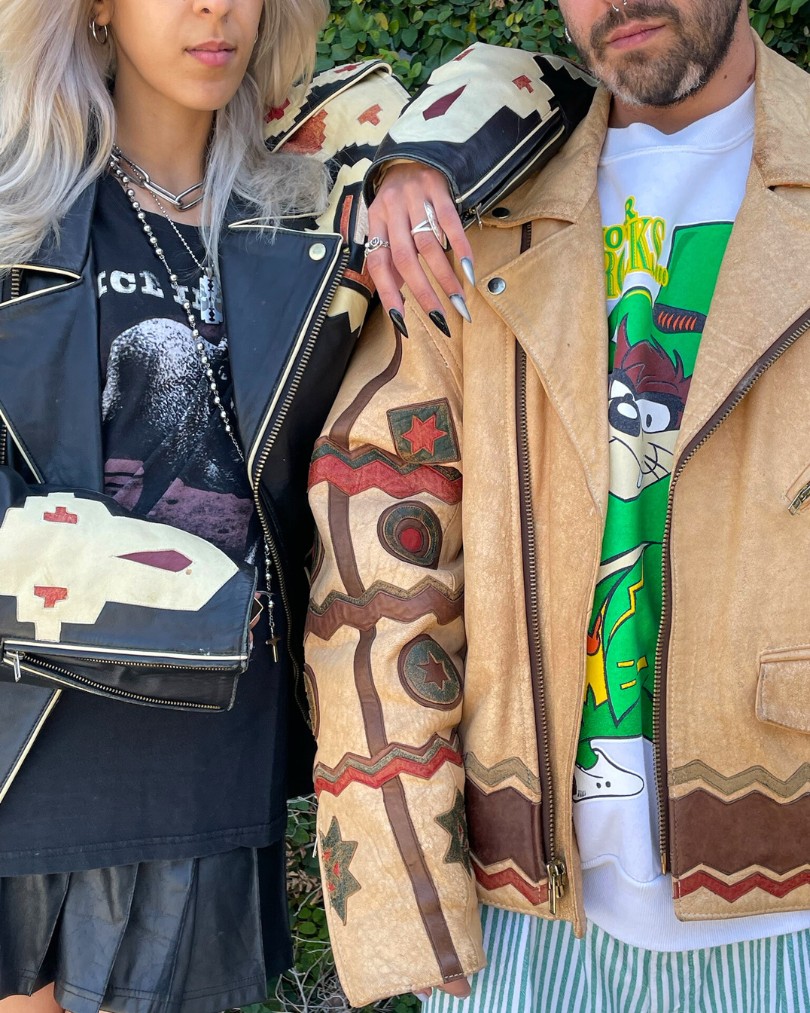 Two people posing outside in vintage leather jackets with western cutouts, styled with modern accents like graphic tee shirts and chunky silver jewelry