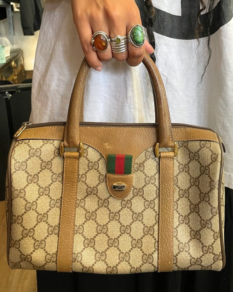 A close up of a hand adorned with chunky sterling silver stone rings carrying a vintage Gucci handbag in their iconic monogram print