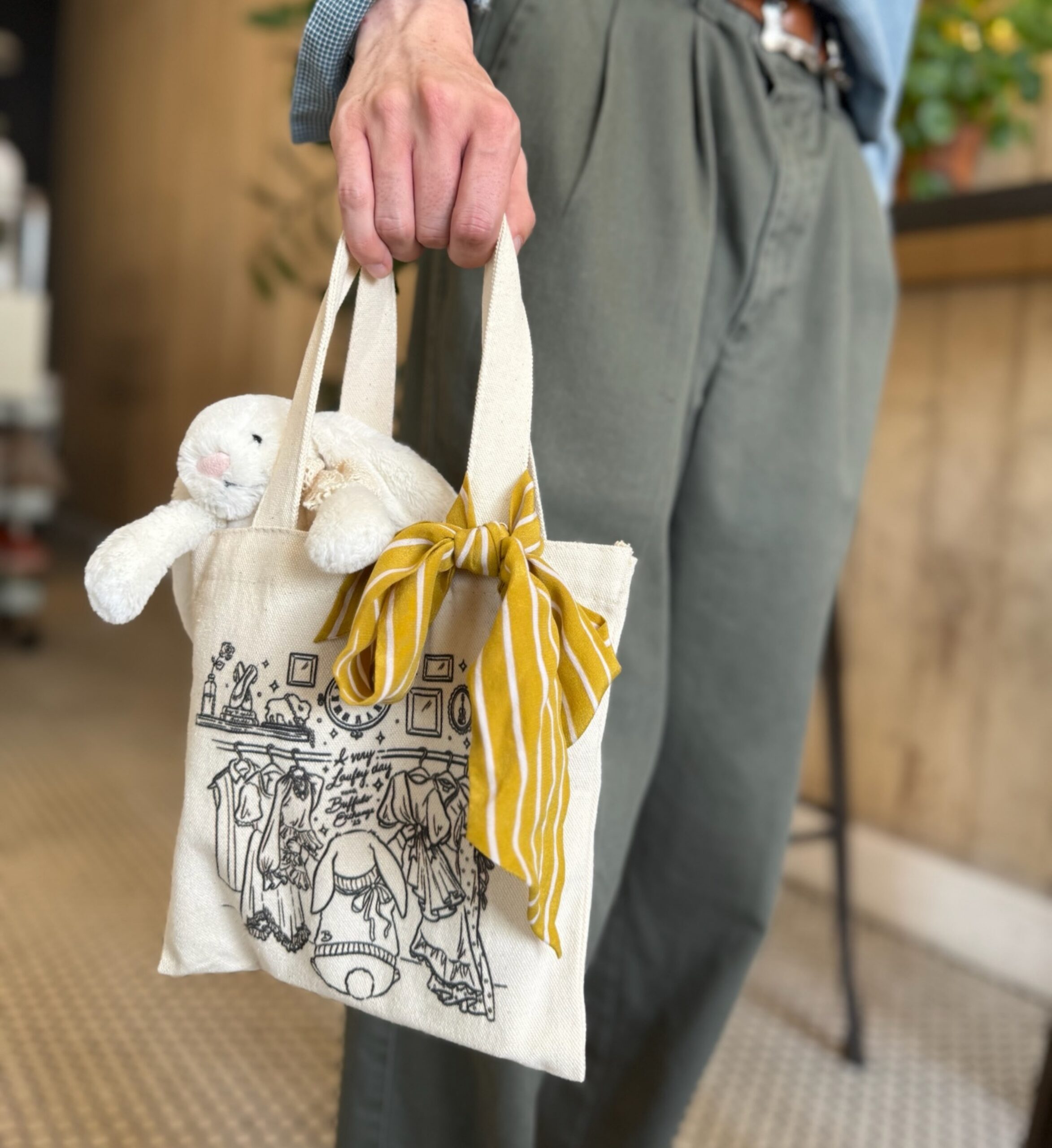 Close-up of person holding exclusive A Very Laufey Day x Buffalo Exchange tote with yellow bow and plus bunny inside
