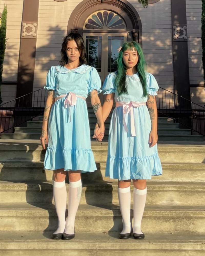 Two people wear matching blue dresses for Halloween costume of The Grady Sisters from The Shining 