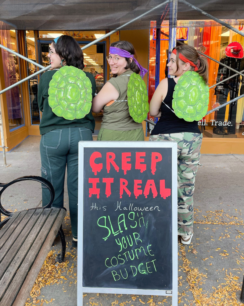 Group of Buffalo employees wearing fake turtle shells on their backs and posing next to a spooky sandwich board