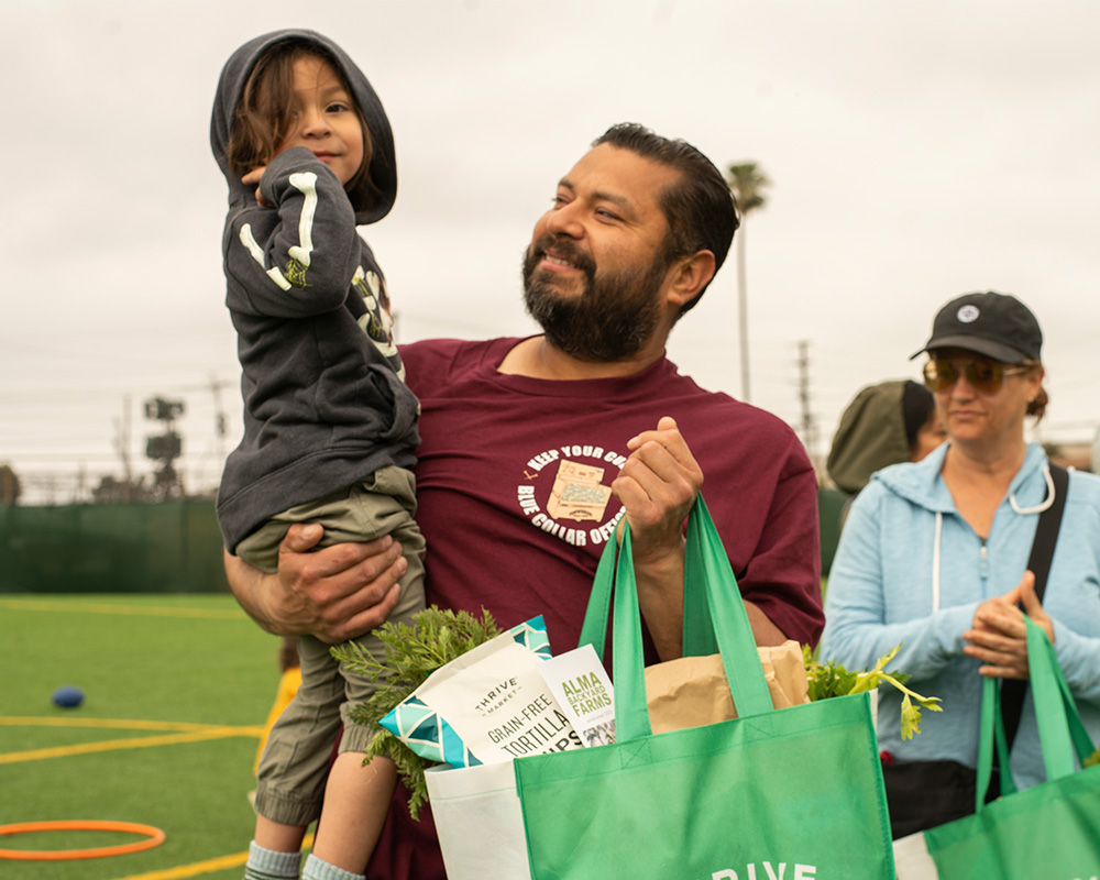 Man smiling and carrying a child and a bag of food.