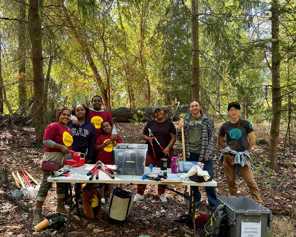 Group photo of Seattle Parks Foundation volunteers in nature with groundskeeping equipment.