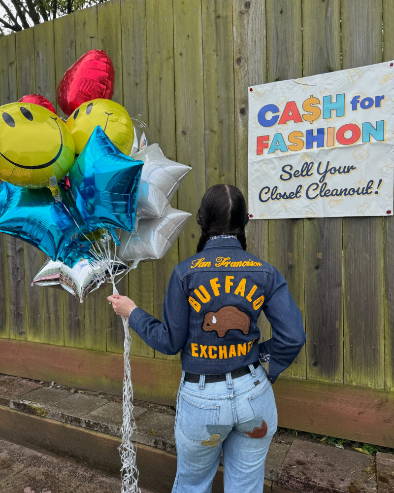 person standing with back to camera holds balloons next to banner that reads "Cash for Fashion, Sell Your Closet Cleanout!"
